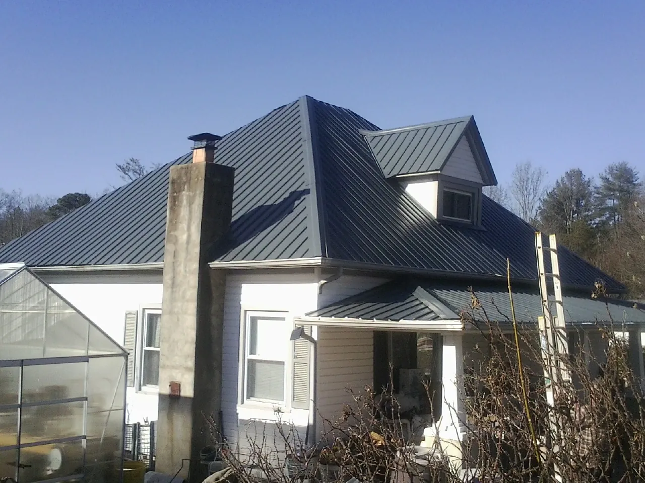 Dark blue standing seam metal roof on a white farmhouse with dormer — Slate & Tile Roof Repair by Roofing Brothers in Barto