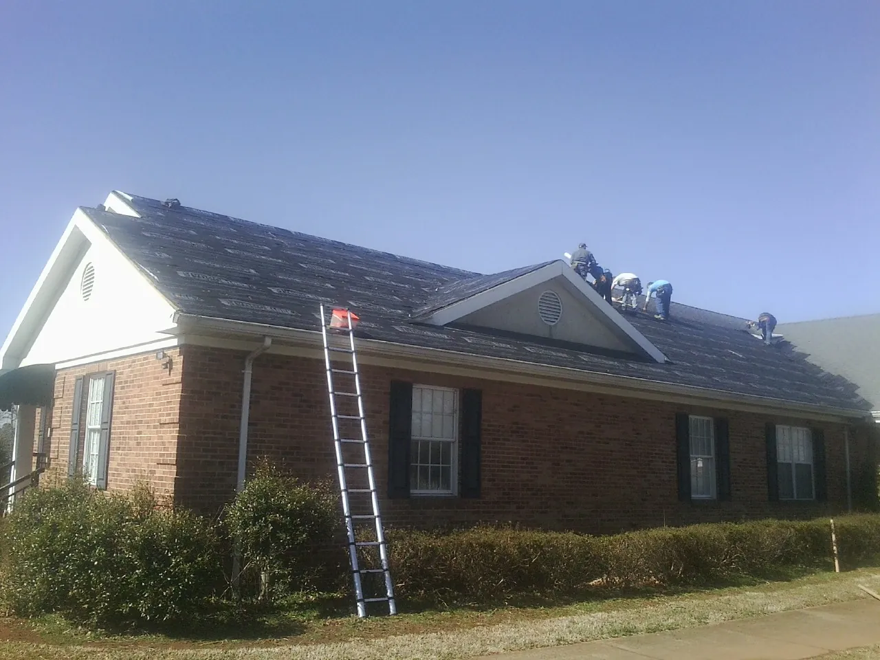 Crew tearing shingles off a brick ranch roof with a ladder set — Metal Roof Repair work by our crew in Barto