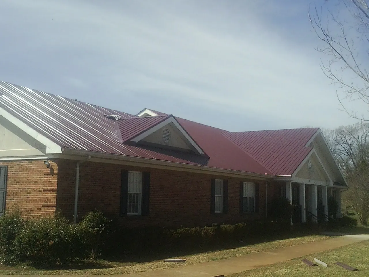 Red metal roof with gabled entries on a long brick building, from a Hail Damage Roof Repair job in Barto