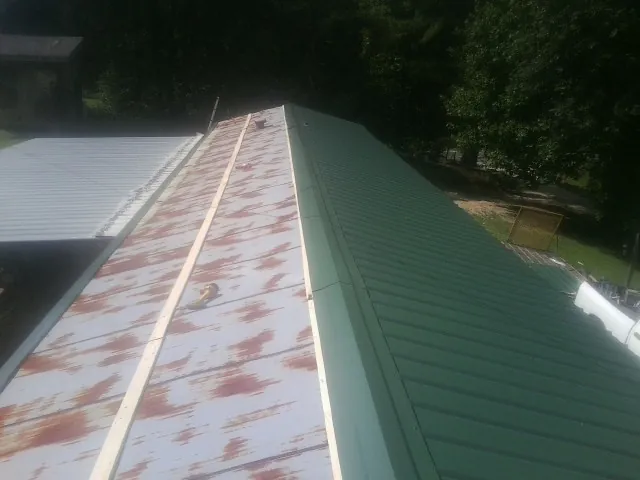 Old rusted panels beside newly installed green metal roofing — Wind Damage Roof Repair by Roofing Brothers in Barto