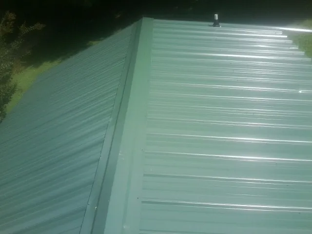 New green metal panels meeting at the ridge of a roof — Flat Roof Repair work by our crew in Barto