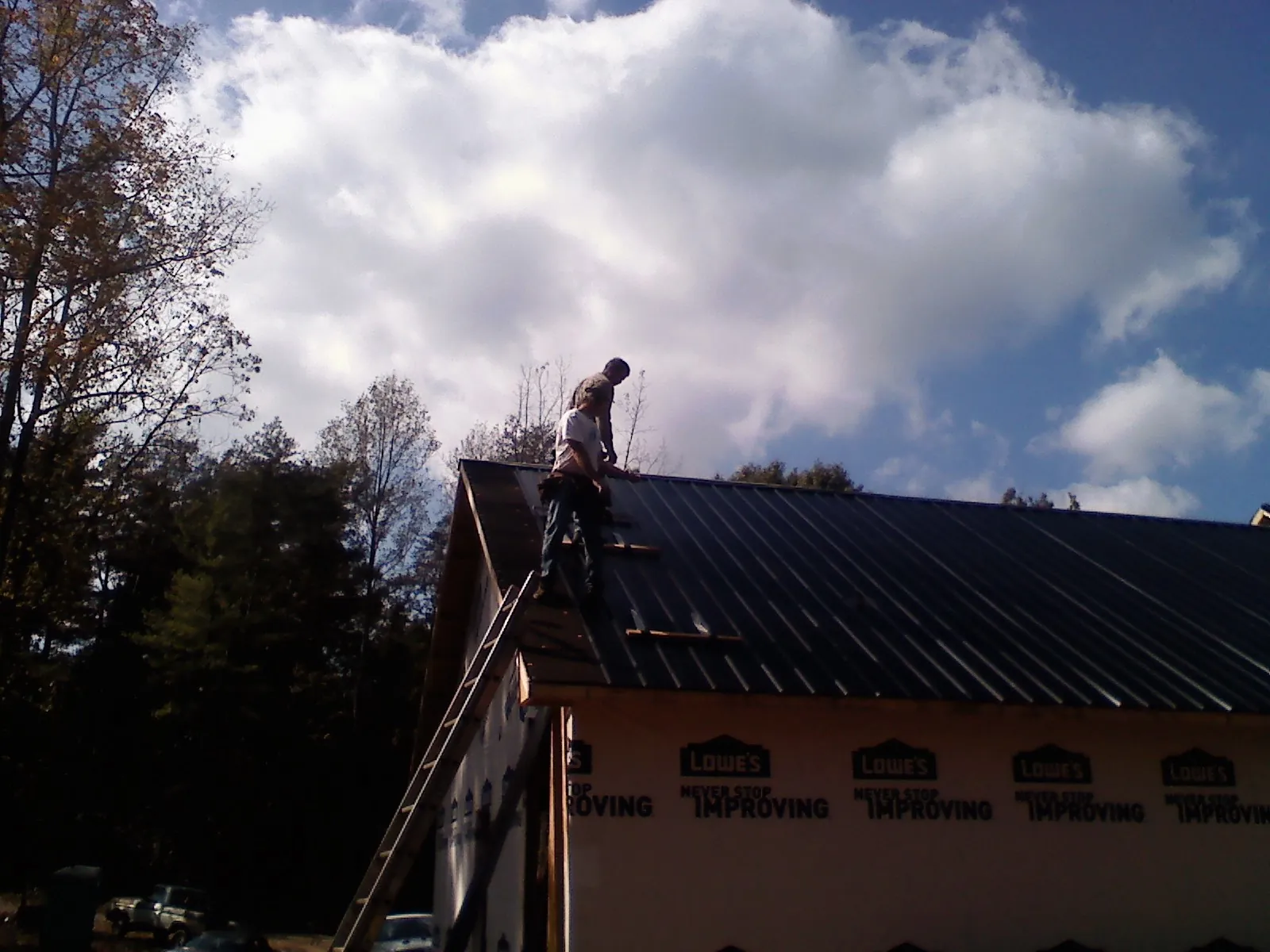 Roofer fastening dark metal panels high against a cloudy sky, from a Roof Inspection job in Barto